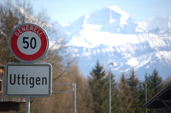 Ortsschild Uttigen mit 50er Tafel und verschneitem Berg im Hintergrund