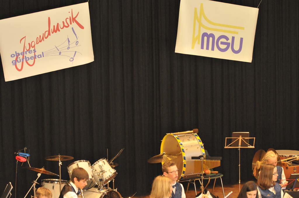 Logos der Jugendmusik und der MGU an rückwärtigen Vorhang auf der Bühne des Mehrzweckgebäudes.