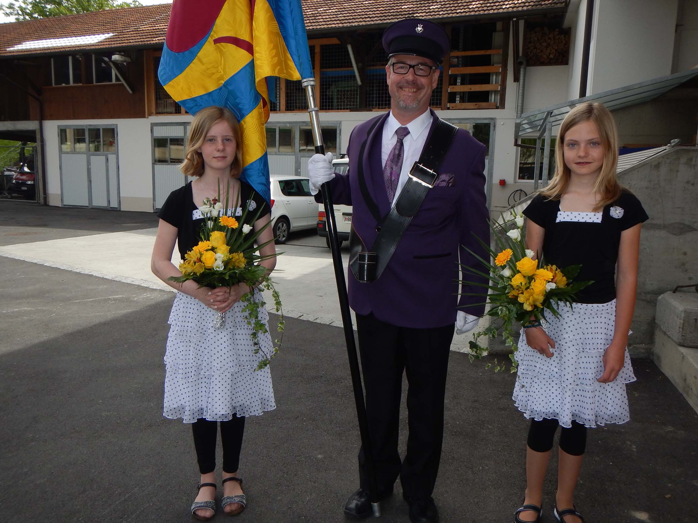 Fähnrich Martin mit den Ehrendamen (Ehrenkindern) Chiara und Lisbeth in schwarz/weissen Kleidchen und mit gelben Blumensträussen.