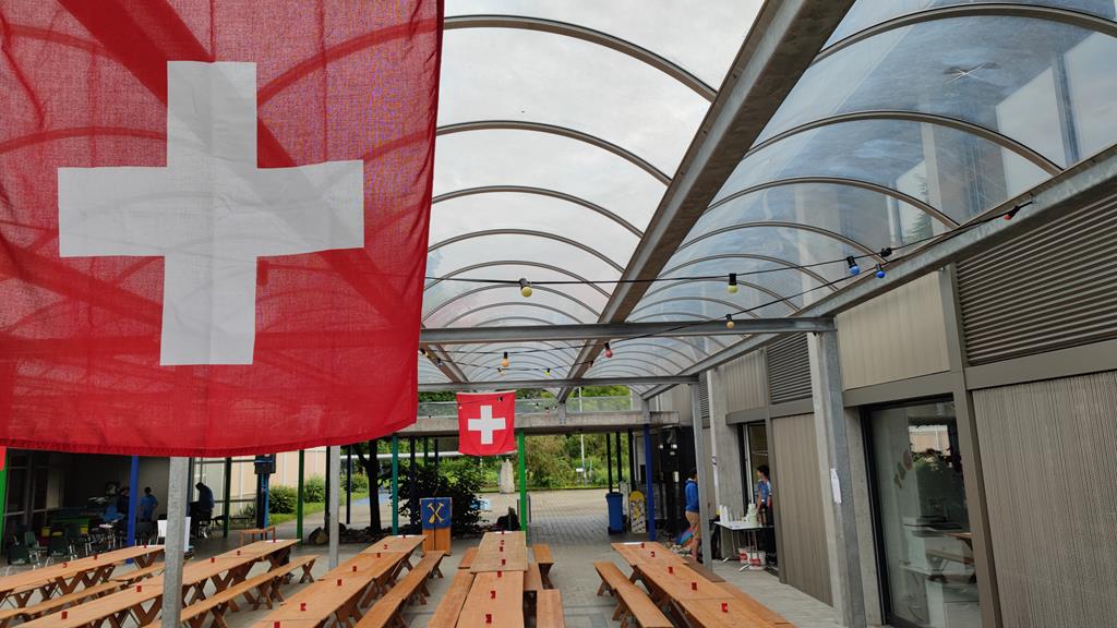 Schweizerfahne und leere Festbänke im Hintergrund unter dem Baldachin des Mehrzweckgebäudes.