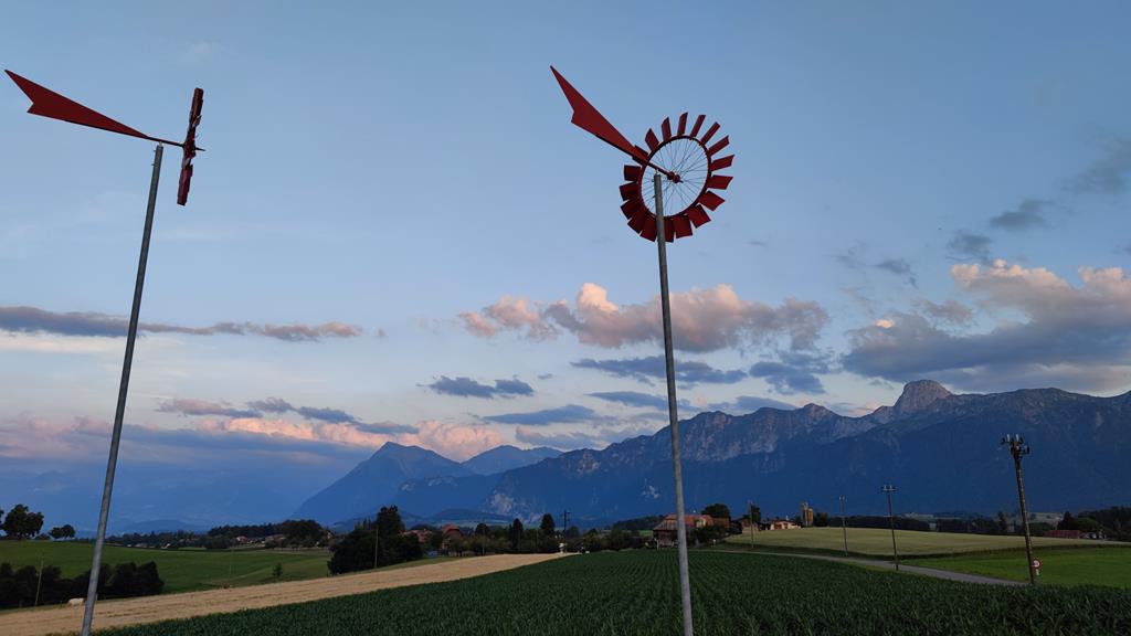 Windrad vor blauem Himmel mit Alpenpanorama.